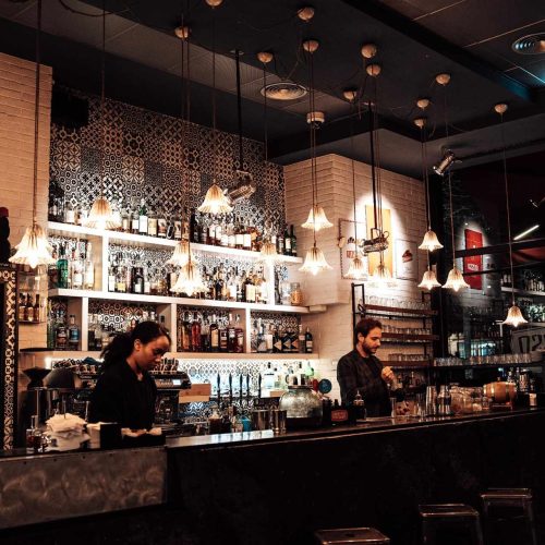 Il bancone del cocktail bar di ROSSO, con lampade a sospensione e bottiglie in mostra