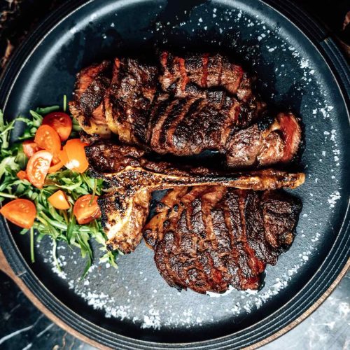 Bistecca con osso e costata alla griglia con rucola e pomodorini, servite su piatto scuro